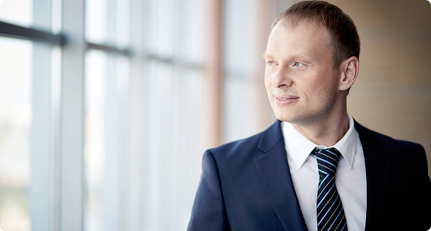 Professionele zakenman in een blauw pak die bij een groot kantoorraam staat, wat zelfvertrouwen, leiderschap en zakelijke professionaliteit vertegenwoordigt.
